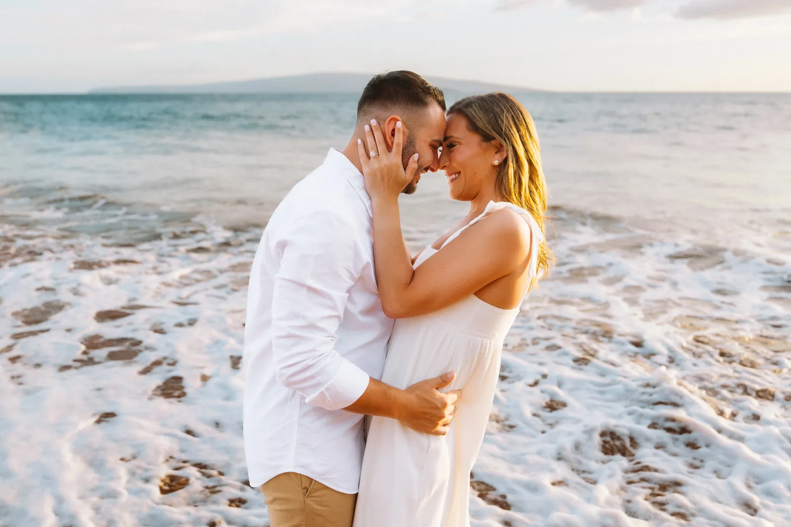 A couple resting forehead to forehead as the surf breaks around them
