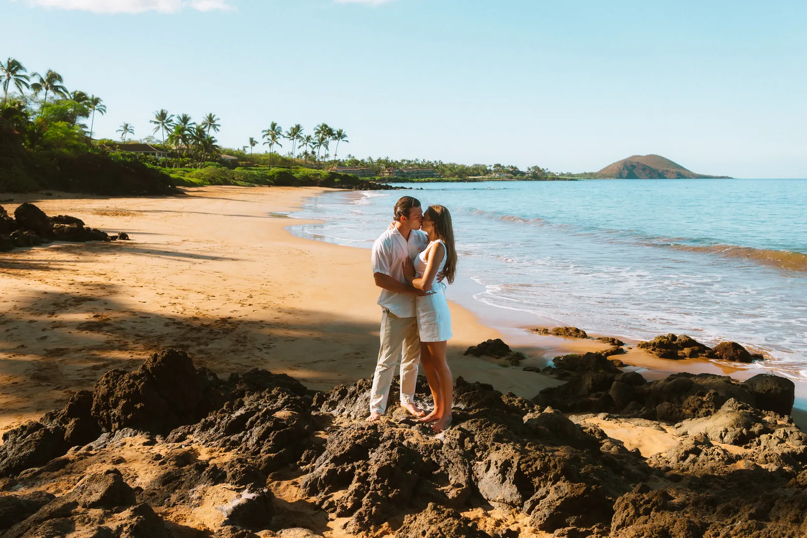 A couple embracing across a lava-rimmed cove, photographed from a distance