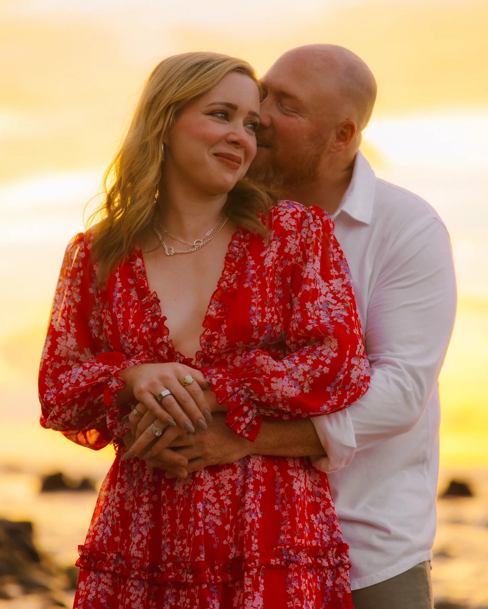 A couple close together at sunset, her red dress catching the last light