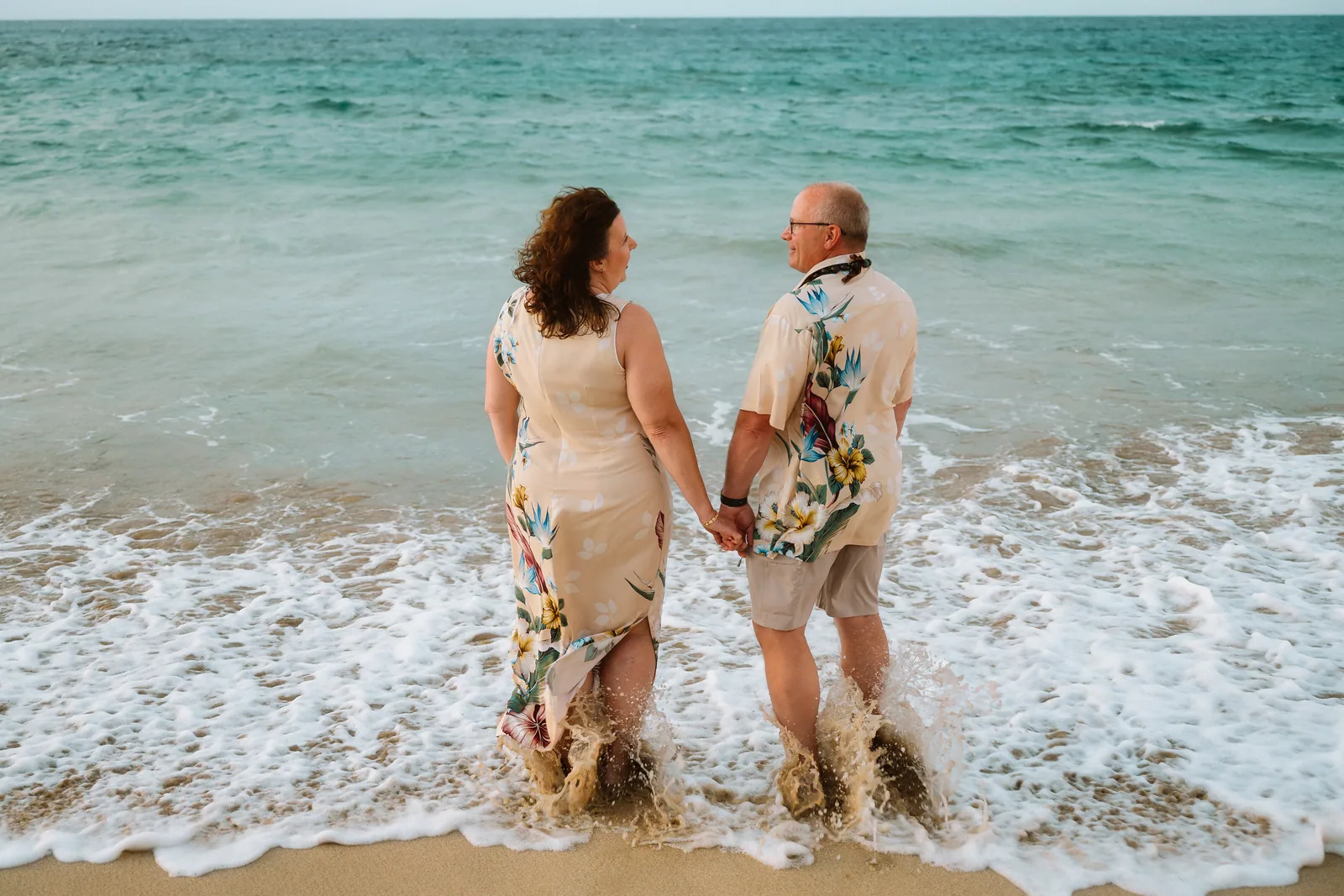 A couple walking through the shallows as a wave washes past their feet