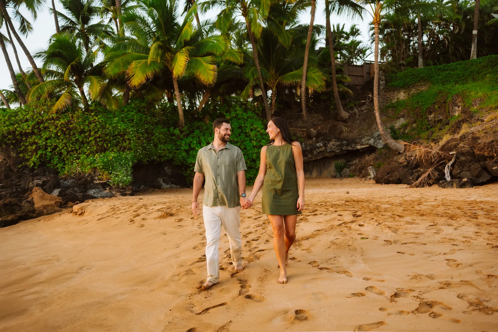 A couple walking the sand hand in hand below a wall of palms