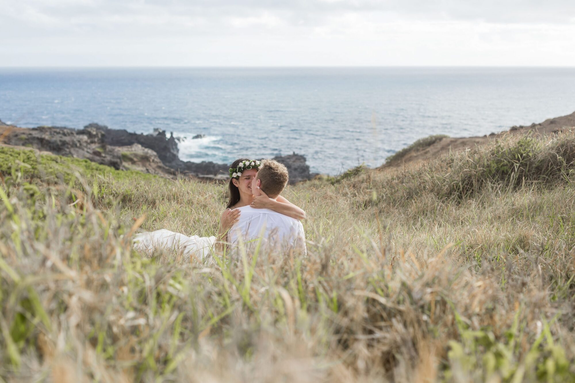 Jessie Hawaii Photography, Couple embracing in tall grass overlooking ocean