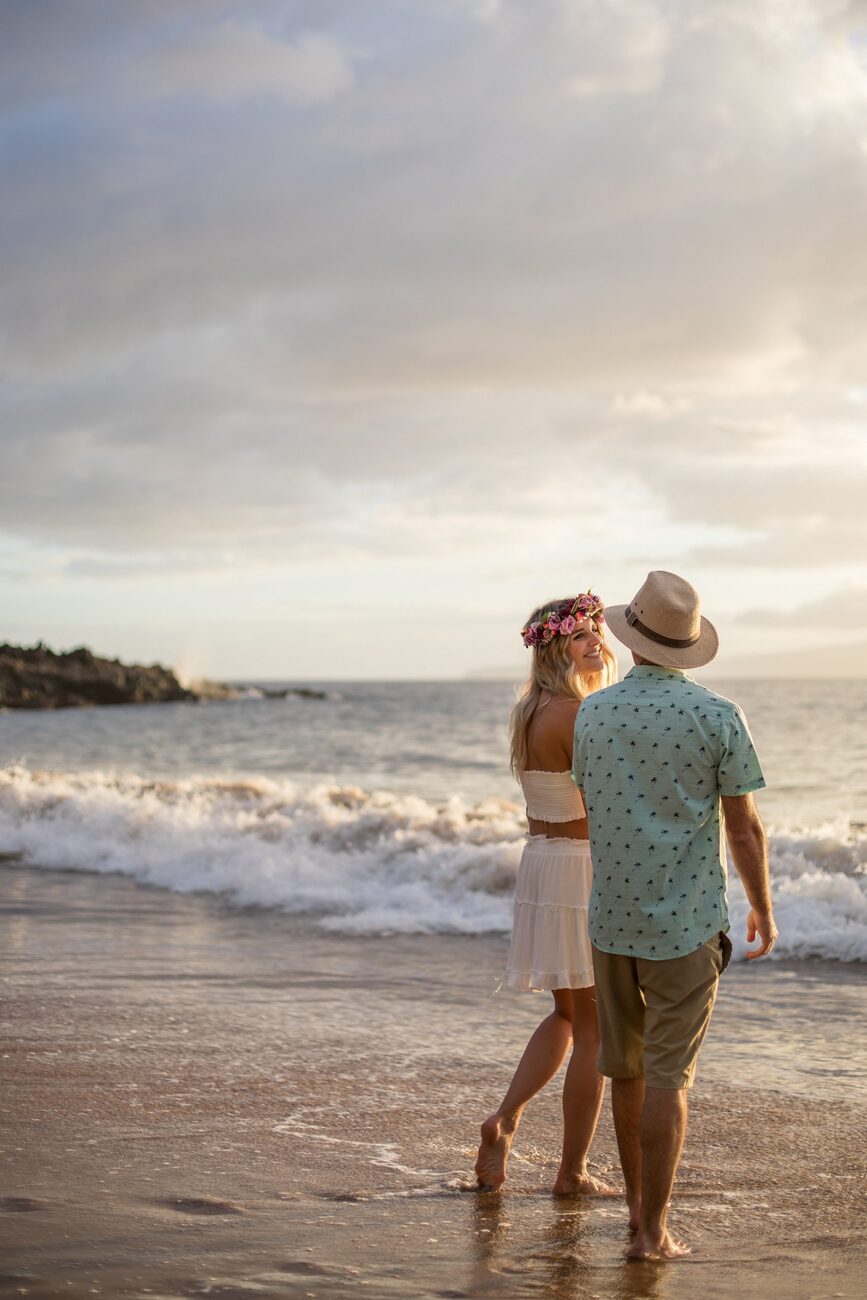 Jessie Hawaii Photography, Couple walking barefoot on a beach at sunset. Woman wears a flower crown.