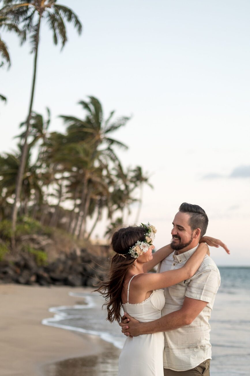 Jessie Hawaii Photography, Happy couple embracing on a beach at sunset, woman wearing a flower crown.