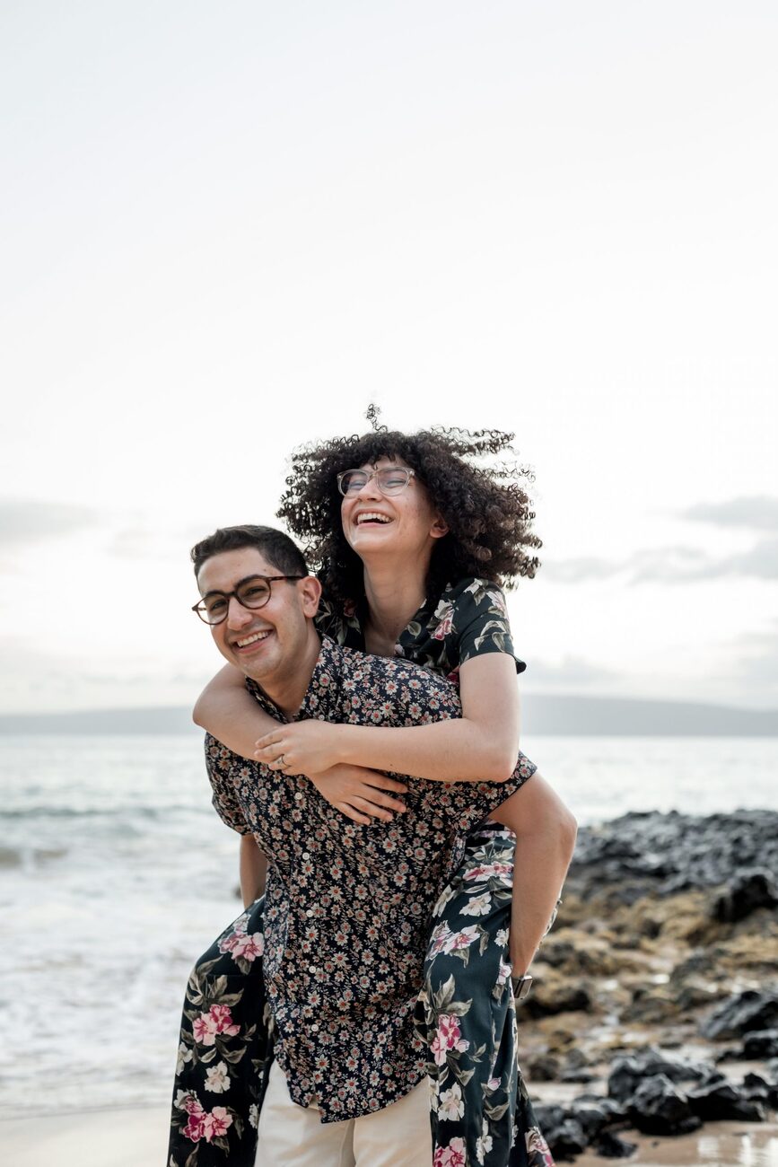 Jessie Hawaii Photography, Happy couple embracing on a beach, woman playfully piggybacking man.