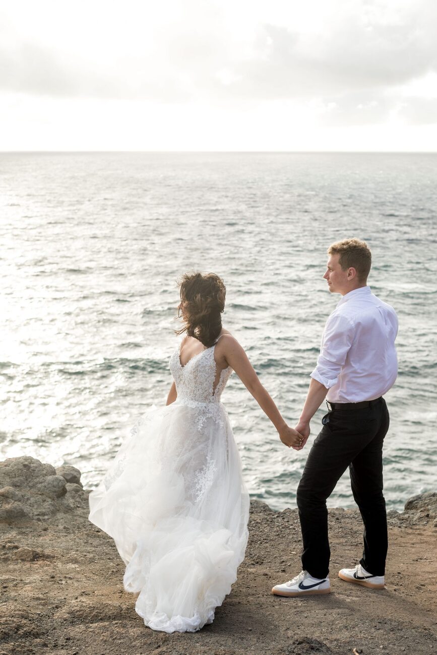 Jessie Hawaii Photography, Bride and groom holding hands on a cliff overlooking the ocean.