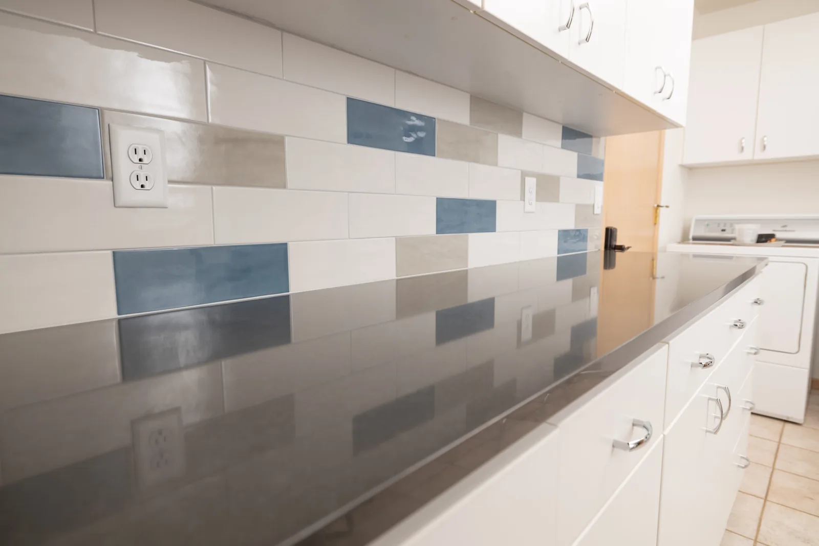 Laundry designed by Kalluna Interior Design — A long quartz run and a rhythm of backsplash tile give a working room a reason to be looked at.
