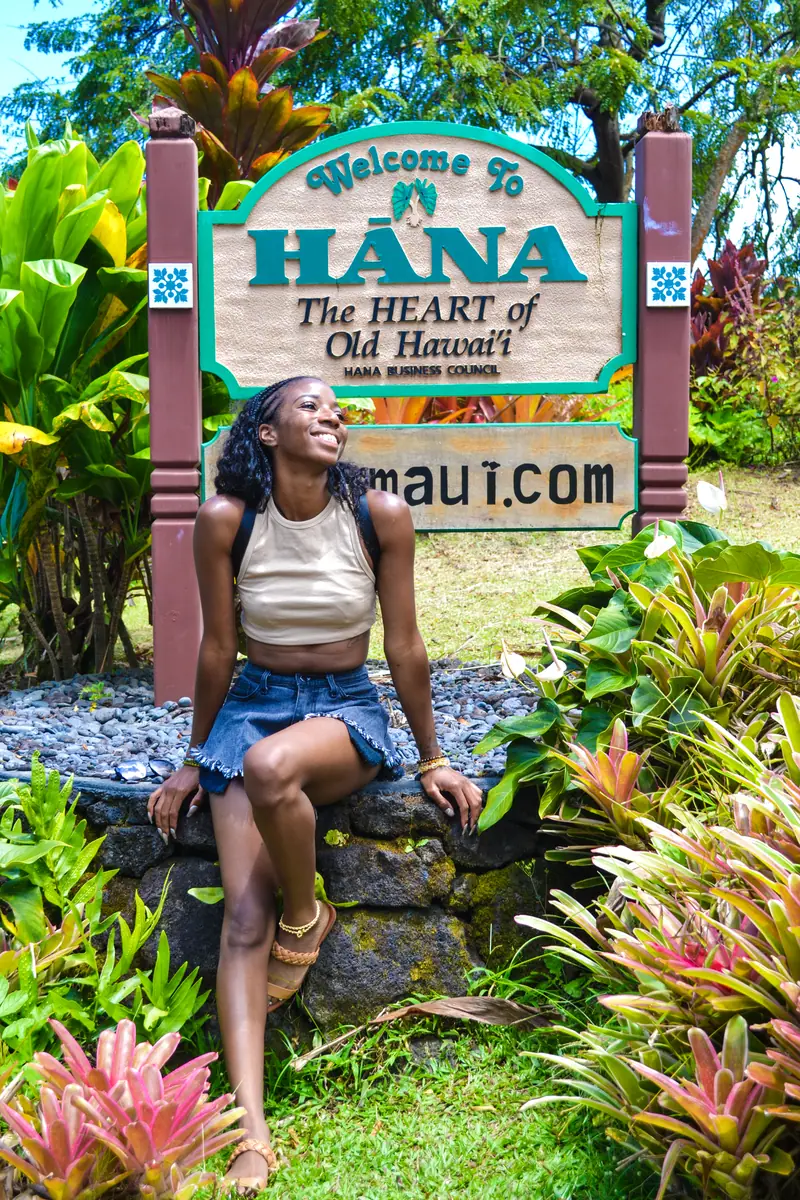 A guest sitting beside the Welcome to Hana sign